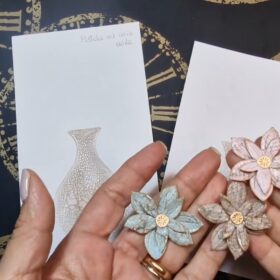 Si vedono in primo piano tre fiori, uno rosa, uno grigio e uno marrone, con l'effetto craklé