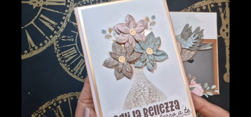 Si vede in primo piano la card finita, con il vaso da fiori con tecnica craklé, tre fiori dentro al vaso e la scritta "cogli la bellezza che vibra intorno a te"